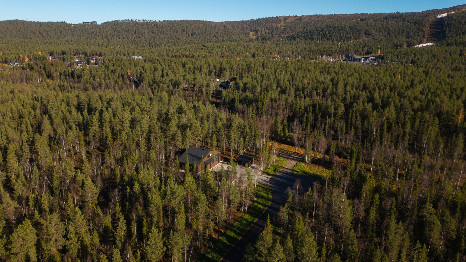 An aerial view across the forest towards the Levi fell, with the ski slopes visible on the horizon and Villa Löhö in the foreground.