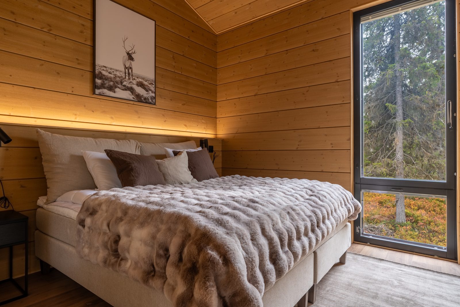 The main bedroom with a double bed made up in linen and fur, beside a window looking into the forest.